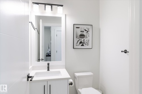 Contemporary bathroom featuring a white vanity with an integrated sink, black hardware, and a framed mirror with overhead lighting - 1214 Eaton Lane, Edmonton, AB - Indoor Photo Showing Bathroom