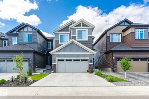 Contemporary two-story exterior featuring a light gray siding facade, a prominent front gable, an attached two-car garage with a light gray door, a concrete driveway, and stone accents on the lower level - 1214 Eaton Lane, Edmonton, AB - Outdoor With Facade