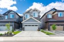 Contemporary two-story exterior featuring a light gray siding facade, a prominent front gable, an attached two-car garage with a light gray door, a concrete driveway, and stone accents on the lower level - 1214 Eaton Lane, Edmonton, AB  - Outdoor With Facade 