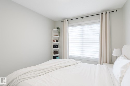Bedroom featuring a window with roller shades, light-toned walls, and a built-in shelving unit - 1214 Eaton Lane, Edmonton, AB - Indoor Photo Showing Bedroom