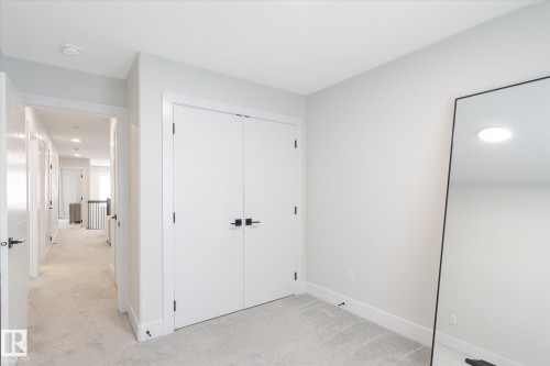 Carpeted interior room featuring a double-door closet with matte black hardware, white trim, and light gray wall paint - 1214 Eaton Lane, Edmonton, AB - Indoor Photo Showing Other Room