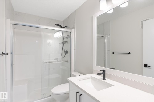 Modern bathroom featuring a single vanity with integrated sink, a solid surface countertop, and matte black fixtures - 1214 Eaton Lane, Edmonton, AB - Indoor Photo Showing Bathroom
