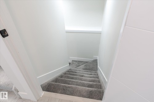 Carpeted staircase with light gray walls, white trim, and a modern white door - 1214 Eaton Lane, Edmonton, AB - Indoor Photo Showing Other Room
