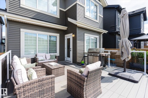 Spacious outdoor deck featuring light-toned composite decking, a clear glass railing system, and direct access to the interior via a white paneled door - 1214 Eaton Lane, Edmonton, AB - Outdoor With Deck Patio Veranda