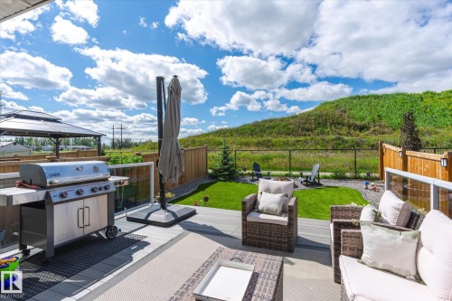 Expansive outdoor living area featuring a multi-level composite deck, glass panel railings, a built-in outdoor kitchen with a grill, a fenced yard with manicured lawn, and a separate gazebo - 1214 Eaton Lane, Edmonton, AB - Outdoor With View