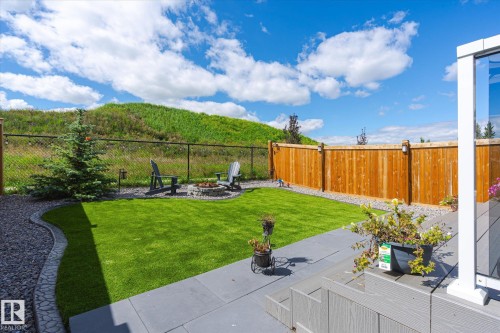 Landscaped backyard featuring a stone fire pit area, manicured lawn, and a light wood privacy fence with integrated lighting - 1214 Eaton Lane, Edmonton, AB - Outdoor