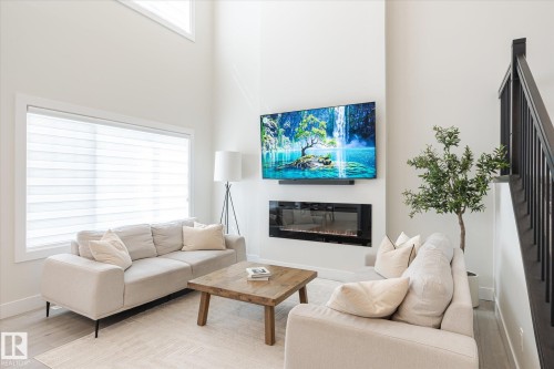 Living area featuring a soaring ceiling, large picture window, light wood-finish flooring, and a built-in electric fireplace - 1214 Eaton Lane, Edmonton, AB - Indoor Photo Showing Living Room With Fireplace