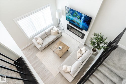 Living room featuring light wood-finish flooring, a contemporary wall-mounted electric fireplace, and expansive windows - 1214 Eaton Lane, Edmonton, AB - Indoor Photo Showing Other Room