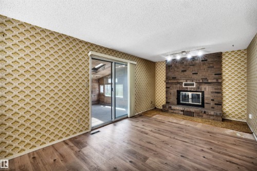 Spacious room featuring wood-finish flooring, a brick fireplace with an insert, and a sliding glass door - 6723 39 Avenue, Edmonton, AB - Indoor With Fireplace