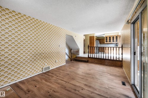 Spacious interior featuring wood-finish flooring, patterned wallpaper, and a slider door - 6723 39 Avenue, Edmonton, AB - 
