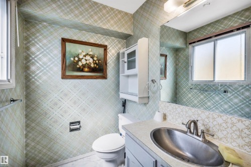 Bathroom featuring patterned wallpaper, a built-in vanity with an oval sink and chrome faucet, a wall-mounted mirror, and a white toilet - 6723 39 Avenue, Edmonton, AB - Indoor Photo Showing Bathroom