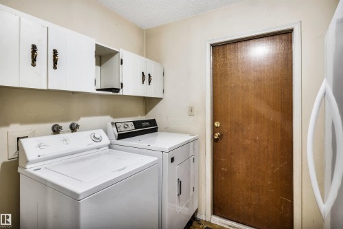 Dedicated laundry area featuring overhead white cabinetry with decorative hardware, a wood-finish door, and a textured ceiling - 6723 39 Avenue, Edmonton, AB - Indoor Photo Showing Laundry Room