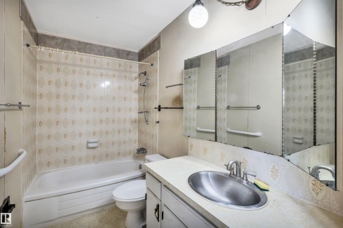 Bathroom featuring a built-in tub with shower, patterned wall tiling, and a vanity with an integrated sink - 6723 39 Avenue, Edmonton, AB - Indoor Photo Showing Bathroom