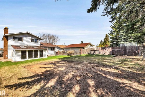 Expansive backyard featuring a large sunroom addition with multiple windows and skylights, a brick chimney, mature evergreen trees, and a wooden perimeter fence - 6723 39 Avenue, Edmonton, AB - Outdoor