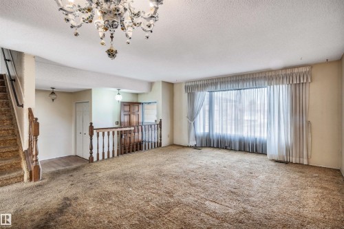 Spacious living area featuring a prominent bay window, a grand chandelier, and a staircase with wood banisters - 6723 39 Avenue, Edmonton, AB - Indoor Photo Showing Other Room