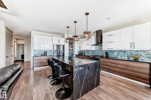 Gourmet kitchen featuring a waterfall island with dark veined stone, stainless steel appliances, wood-finish flooring, white upper cabinetry, and wood-finish lower cabinetry - 5263 47 Ave, Calmar, AB - Indoor Photo Showing Kitchen With Upgraded Kitchen