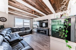 Living area featuring a striking wood-panel ceiling with exposed white beams, wood-finish flooring, and a large picture window - 