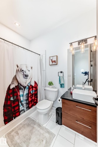 Bathroom featuring a wood-finish vanity with a dark countertop and vessel sink, white tile flooring, a shower with a curtain rod, and a toilet - 5263 47 Ave, Calmar, AB - Indoor Photo Showing Bathroom