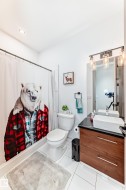 Bathroom featuring a wood-finish vanity with a dark countertop and vessel sink, white tile flooring, a shower with a curtain rod, and a toilet - 