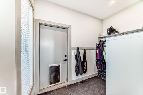 Utility space featuring a side-lite window with horizontal blinds, a neutral-toned door, dark flooring, and built-in wall hooks - 5263 47 Ave, Calmar, AB - Indoor