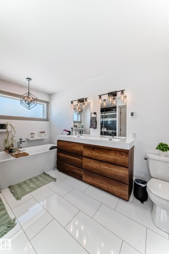 Bathroom featuring a freestanding soaking tub, a dual vanity with wood-finish cabinetry, a white countertop with integrated sinks, and white rectangular floor tiles - 5263 47 Ave, Calmar, AB - Indoor Photo Showing Bathroom