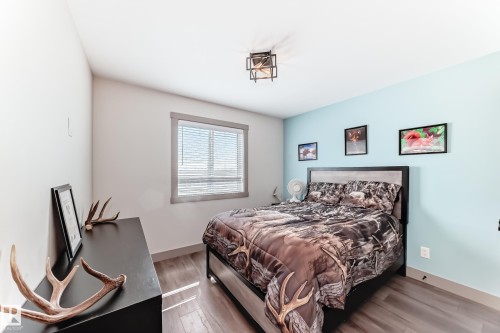 Bedroom featuring wood-finish flooring, a contemporary ceiling light fixture, a window with horizontal blinds, and a two-tone accent wall - 5263 47 Ave, Calmar, AB - Indoor Photo Showing Bedroom