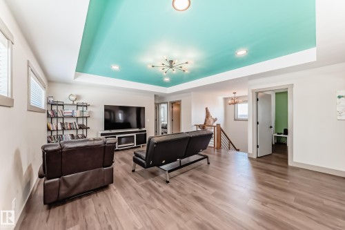 Spacious living area featuring wood-finish flooring, a recessed turquoise ceiling with integrated lighting and a modern chandelier, and a built-in media console - 5263 47 Ave, Calmar, AB - Indoor