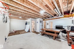 Unfinished basement with exposed wood joists and ductwork, featuring a partial wall enclosure housing a bathroom and a separate door leading to an additional space - 