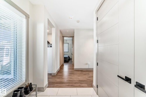 Bright entry area featuring a large window with white blinds, contemporary white doors with black hardware, recessed lighting, and wood-finish flooring transitioning to light-toned tile - 5263 47 Ave, Calmar, AB - Indoor Photo Showing Other Room