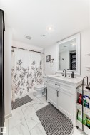 Contemporary bathroom featuring large format tile flooring, a white vanity with shaker-style cabinetry, and a rectangular mirror with a white frame - 