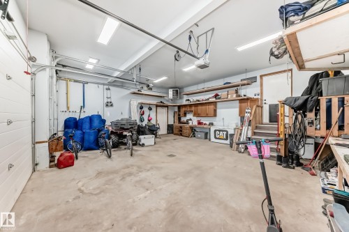 Spacious garage featuring concrete flooring, overhead fluorescent lighting, built-in wooden shelving, and an integrated workbench with cabinetry - 5263 47 Ave, Calmar, AB - Indoor Photo Showing Garage