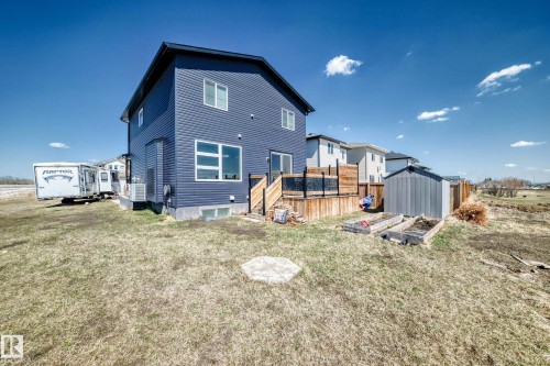 Modern two-story residence featuring blue horizontal siding, a rear wood deck with dark railing, a shed, and raised garden beds - 5263 47 Ave, Calmar, AB - Outdoor
