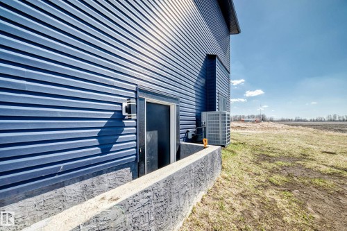 Navy blue corrugated metal siding exterior featuring a built-in exterior door, a concrete window well, and an exposed HVAC condenser unit - 5263 47 Ave, Calmar, AB - Outdoor