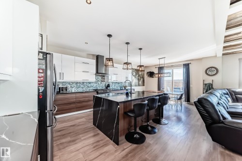 Modern kitchen featuring an expansive center island with waterfall countertop, stainless steel appliances, and a mosaic tile backsplash - 5263 47 Ave, Calmar, AB - Indoor Photo Showing Kitchen
