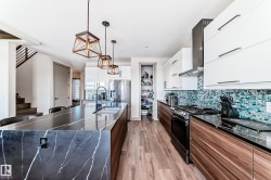 Spacious kitchen featuring a large island with waterfall countertop, stainless steel appliances, wood-finish flooring, a mosaic tile backsplash, and contemporary pendant lighting - 