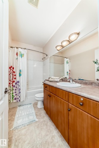 Bathroom featuring a single vanity with wood-finish cabinetry, a large vanity mirror, a three-light fixture, and a shower-tub combination with white tile surround - 40 13808 155 Avenue, Edmonton, AB - Indoor Photo Showing Bathroom