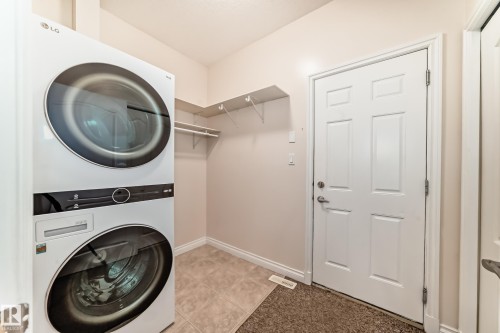 Dedicated laundry area featuring a stacked washer and dryer, tile flooring, and integrated shelving - 40 13808 155 Avenue, Edmonton, AB - Indoor Photo Showing Laundry Room