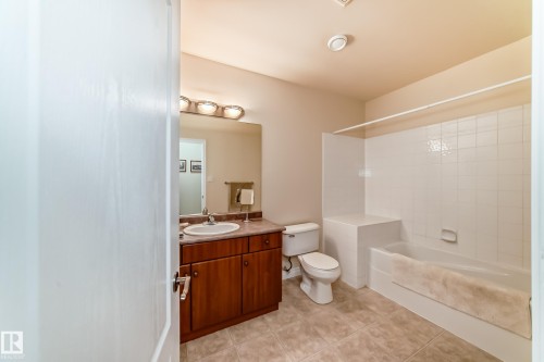 Bathroom featuring a wood-finish vanity with an integrated sink, a large mirror, and three-light fixture - 40 13808 155 Avenue, Edmonton, AB - Indoor Photo Showing Bathroom