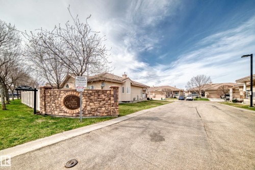 Community entrance featuring a stone monument sign, manicured grass, and a white privacy fence - 40 13808 155 Avenue, Edmonton, AB - Outdoor