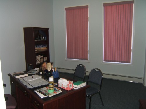 Room featuring two windows with vertical blinds, light-colored walls, and dark carpeting - 4707 50 Street, Two Hills, AB - Indoor Photo Showing Office