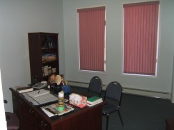 Room featuring two windows with vertical blinds, light-colored walls, and dark carpeting - 