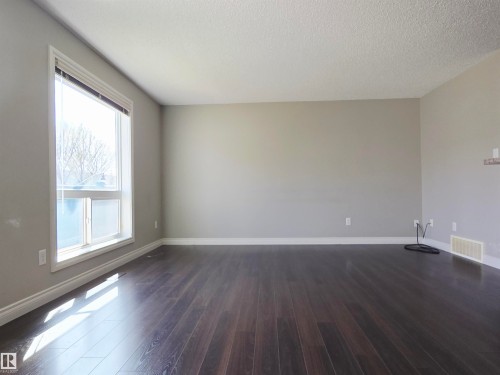 Spacious room featuring dark laminate flooring, light grey painted walls, white trim, and a large window with white framing - 21321 94 Avenue, Edmonton, AB - Indoor Photo Showing Other Room