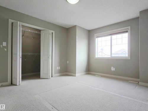 Spacious room featuring neutral carpeting, light gray walls, a window with white trim, and a built-in closet with bifold doors and wire shelving - 21321 94 Avenue, Edmonton, AB - Indoor
