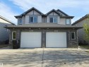 Contemporary duplex exterior featuring a stone and siding facade, two integrated single-car garages, an asphalt shingle roof, and multiple upper-level windows - 21321 94 Avenue, Edmonton, AB  - Outdoor 