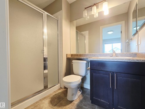 Ensuite featuring a shower with frosted glass doors, a dark wood-finish vanity with a single sink, a speckled countertop, and lino flooring - 21321 94 Avenue, Edmonton, AB - Indoor Photo Showing Bathroom