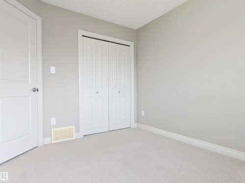 Carpeted room featuring a bifold closet door, a paneled interior door with a silver knob, light gray walls, white baseboards, and a ceiling with a textured finish - 21321 94 Avenue, Edmonton, AB - Indoor