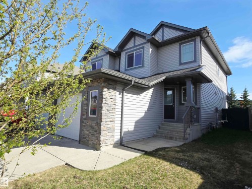 Two-story residence featuring gray siding with darker trim accents, an attached garage, and a covered front entry with stone veneer detailing - 21321 94 Avenue, Edmonton, AB - Outdoor