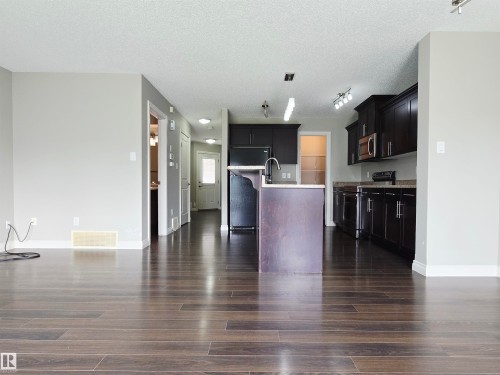 Open-concept living space featuring laminate flooring, a kitchen island with sink, dark wood cabinetry, and stainless steel appliances - 21321 94 Avenue, Edmonton, AB - Indoor Photo Showing Kitchen