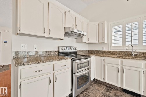 Kitchen featuring white cabinetry, stone-finish countertops with matching backsplash, stainless steel range with double ovens, and a stainless steel sink with a gooseneck faucet - 18903 70 Avenue, Edmonton, AB - Indoor Photo Showing Kitchen