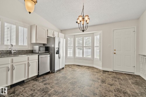 Eat-in kitchen featuring white cabinetry, granite countertops, stainless steel appliances, and a bay window with plantation shutters - 18903 70 Avenue, Edmonton, AB - Indoor Photo Showing Kitchen
